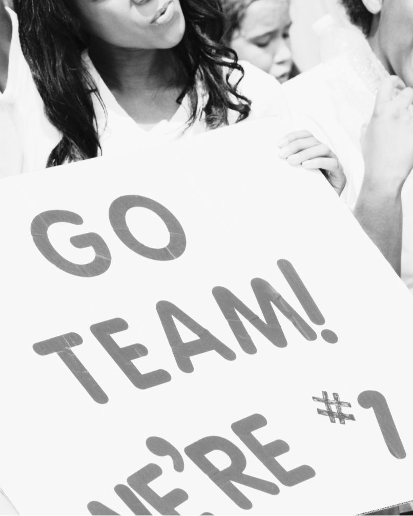 Woman holding a 'Go Team! We're #1' sign in a crowd